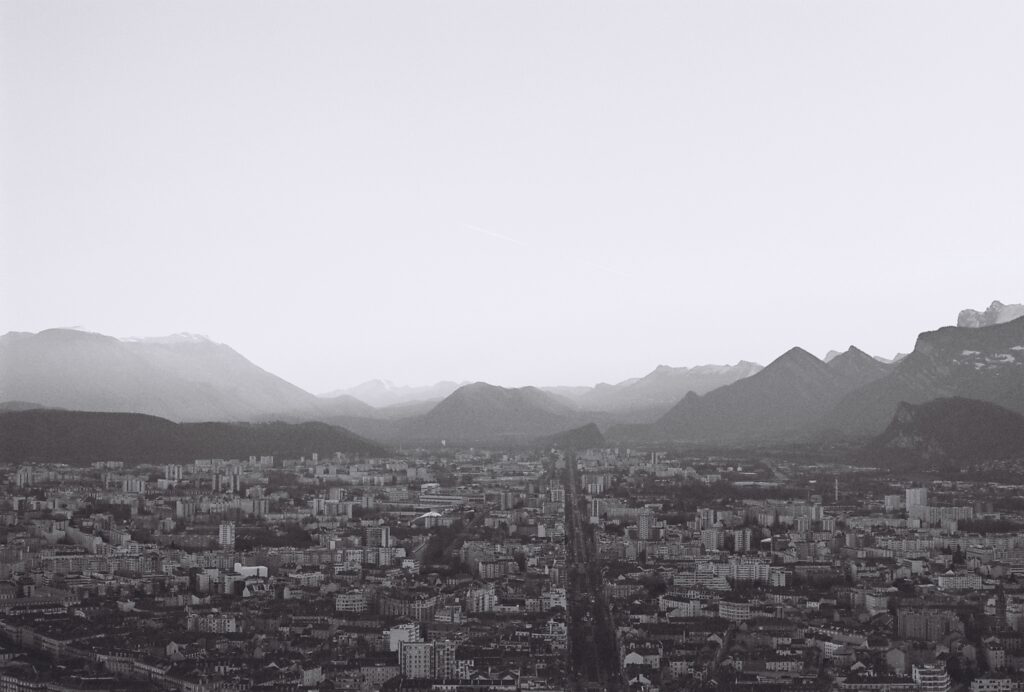 Ville C'est une photo de la ville de grenoble en noir et blanc. Elle sert à montrer un écosystème, un centre urbain, où il y a des enjeux sociaux, des initiatives d'innovation sociale.